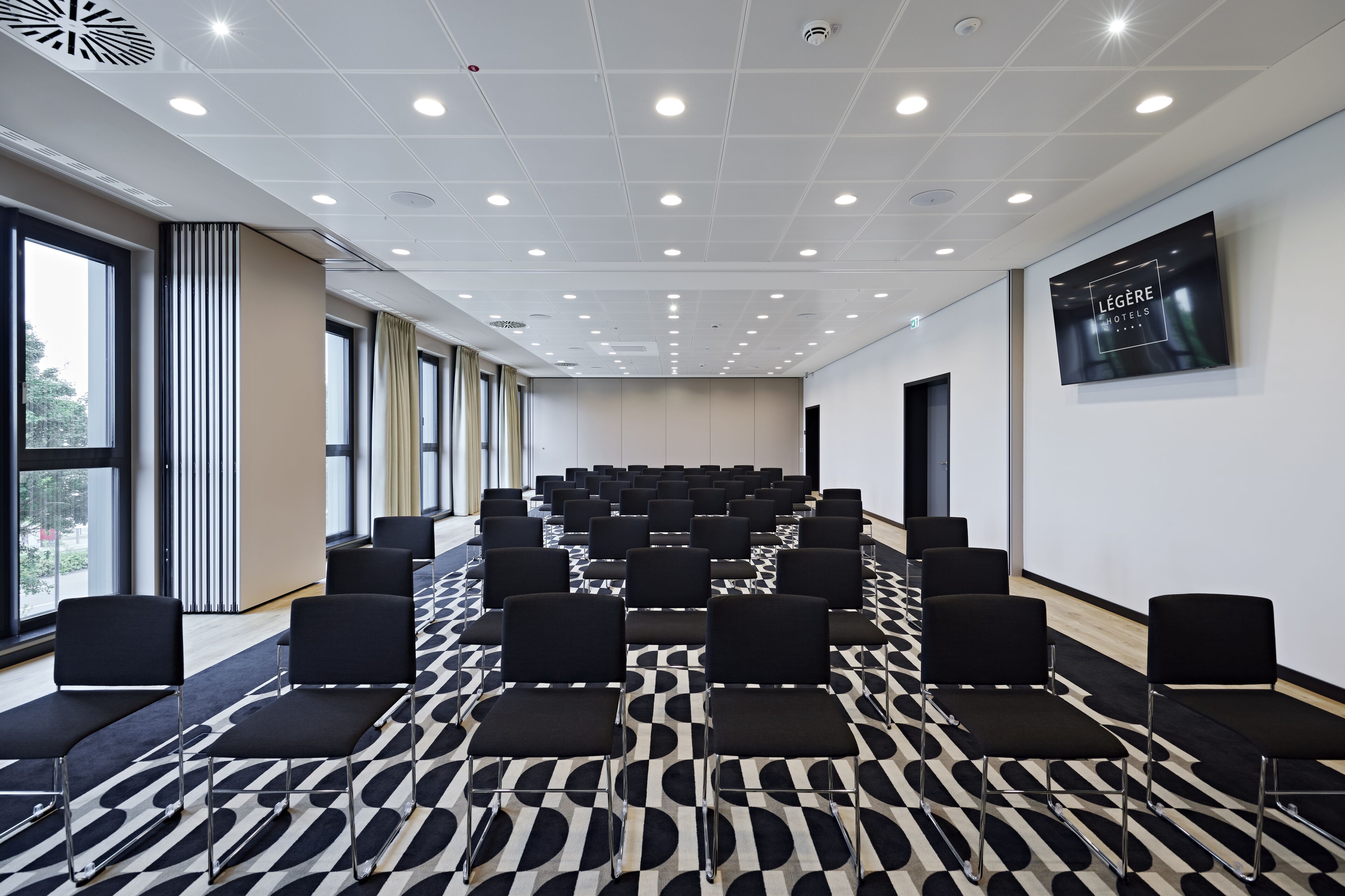 A conference room with rows of black chairs, a patterned carpet, and a large window on one side.