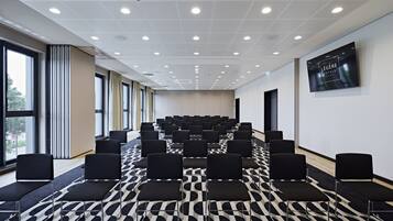 Une salle de conférence avec des rangées de chaises noires, une moquette à motifs et une grande fenêtre sur un des murs.