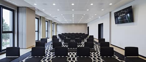 A conference room with rows of black chairs, a patterned carpet, and a large window on one side.