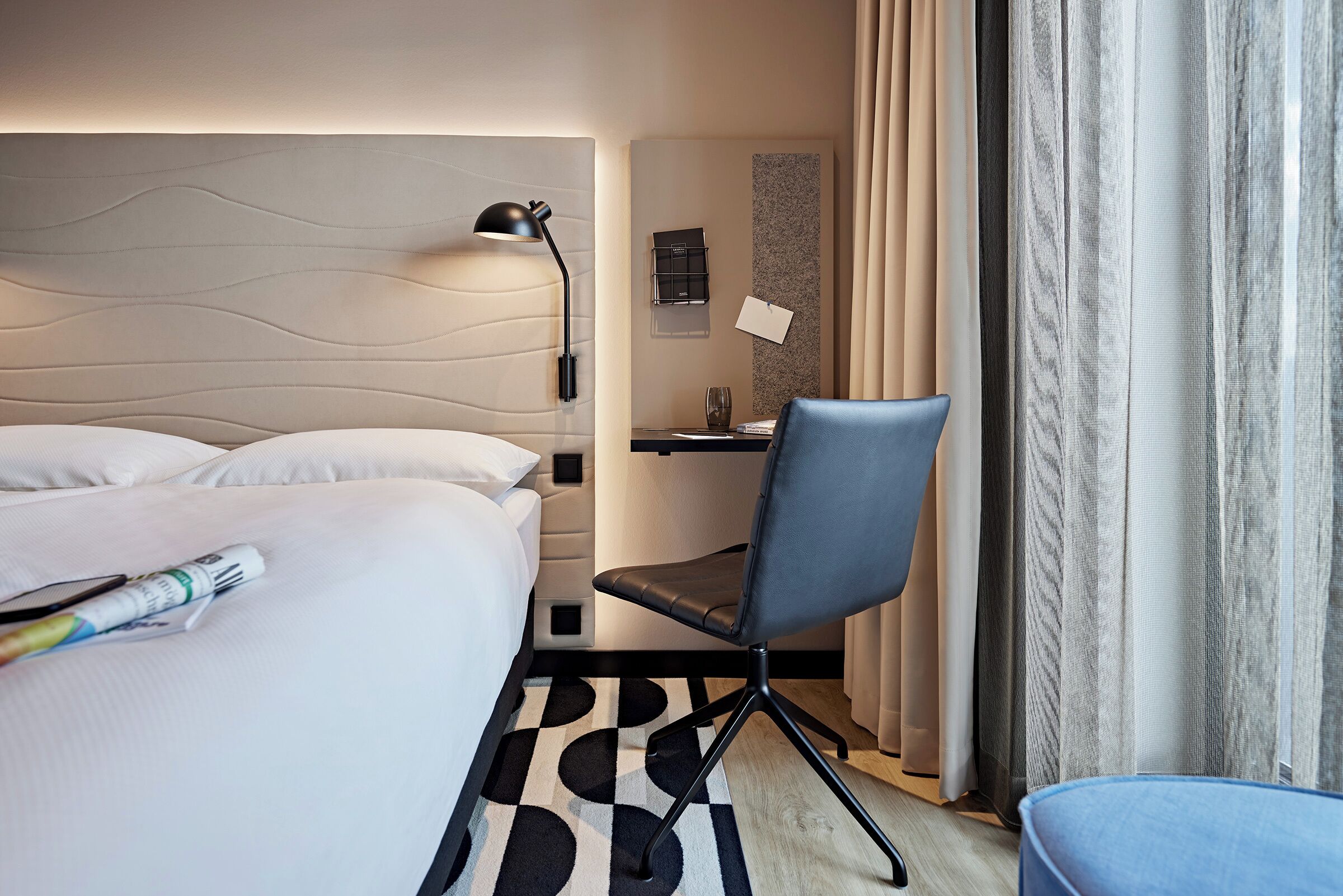 A hotel room with a bed, a desk, a chair, and a window with curtains.