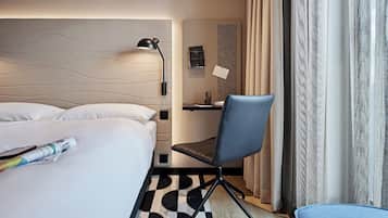 A hotel room with a bed, a desk, a chair, and a window with curtains.