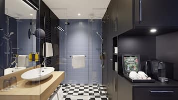 Un baño moderno con piso a cuadros, cabina de ducha de vidrio, lavamanos con espejo y una cafetera.
