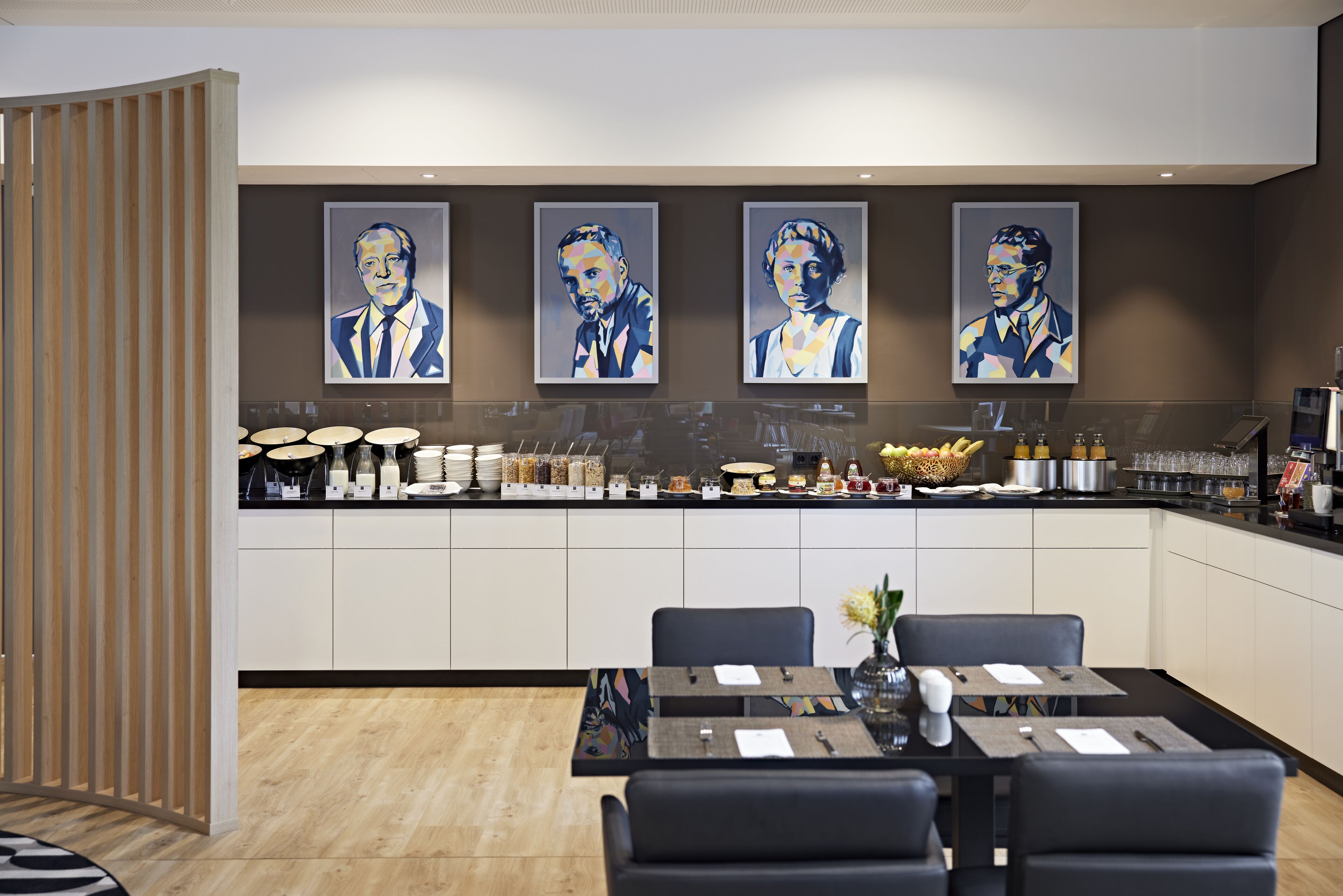 Una cocina moderna con una isla central, un comedor con sillas negras y cuatro retratos enmarcados en la pared.