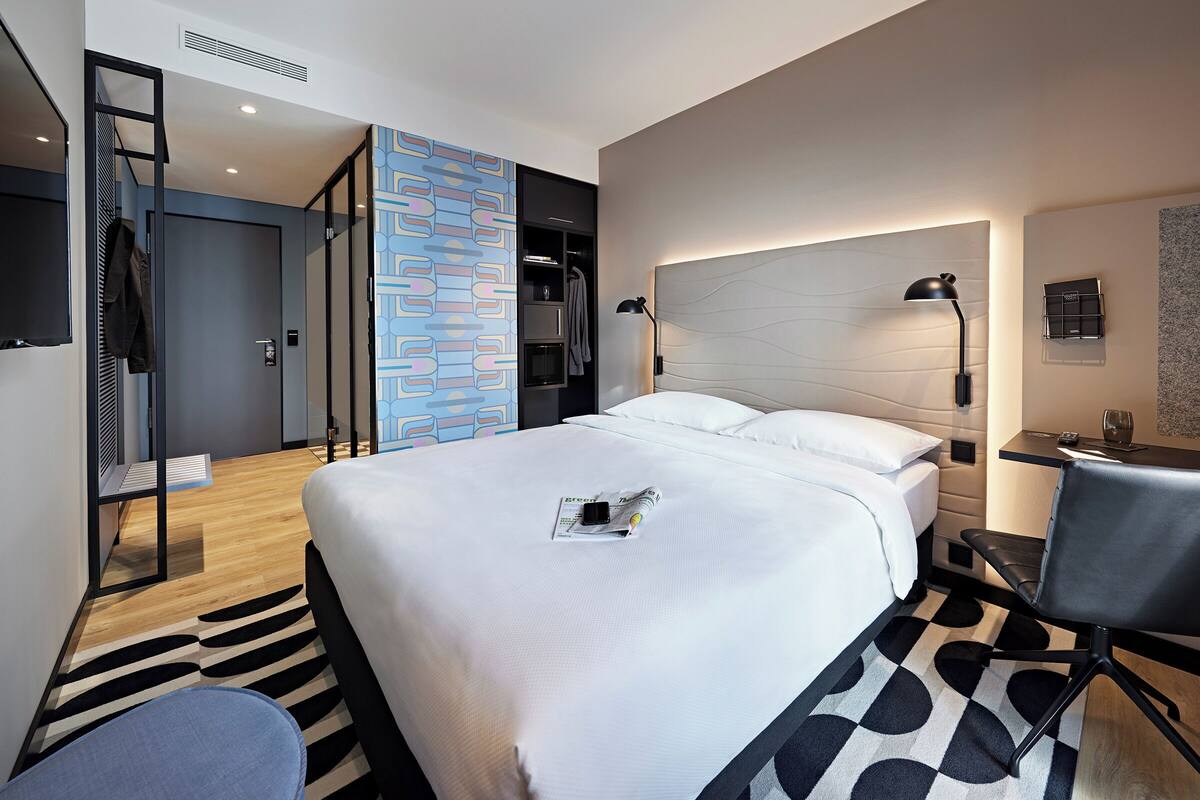 Una habitación de hotel moderna con una cama grande, un escritorio, una silla y un armario.