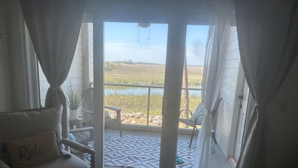 Ett rum med utsikt över en vattenyta och en gräsklädd äng, med en skjutdörr i glas.