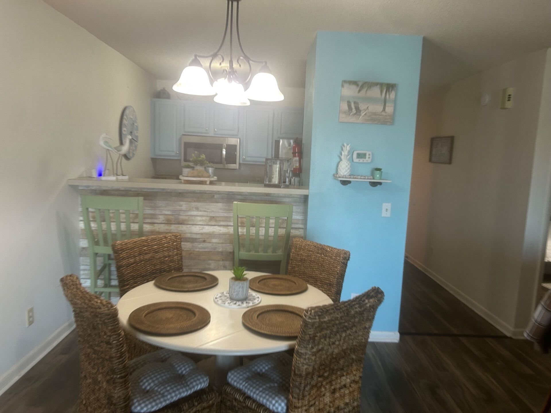 A dining area with a round table, wicker chairs, and a hanging light fixture.