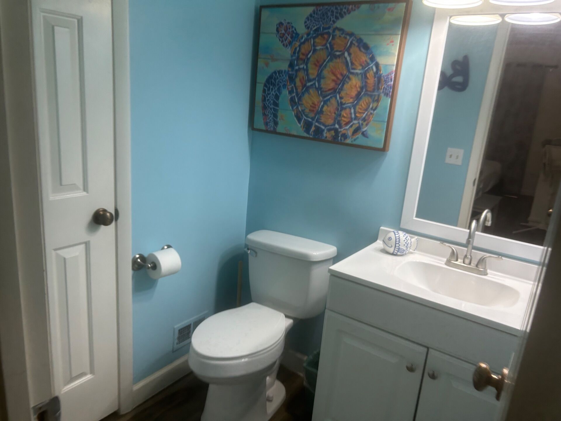 A bathroom with a toilet, sink, and a painting of a turtle on the wall.