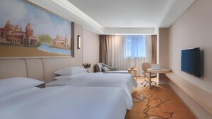 Hotellihuone, jossa on kaksi sänkyä, työpöytä, tuoli, televisio ja taulu seinällä.