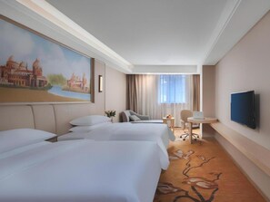 Quarto de hotel com duas camas, uma escrivaninha, uma cadeira, uma televisão e um quadro na parede.