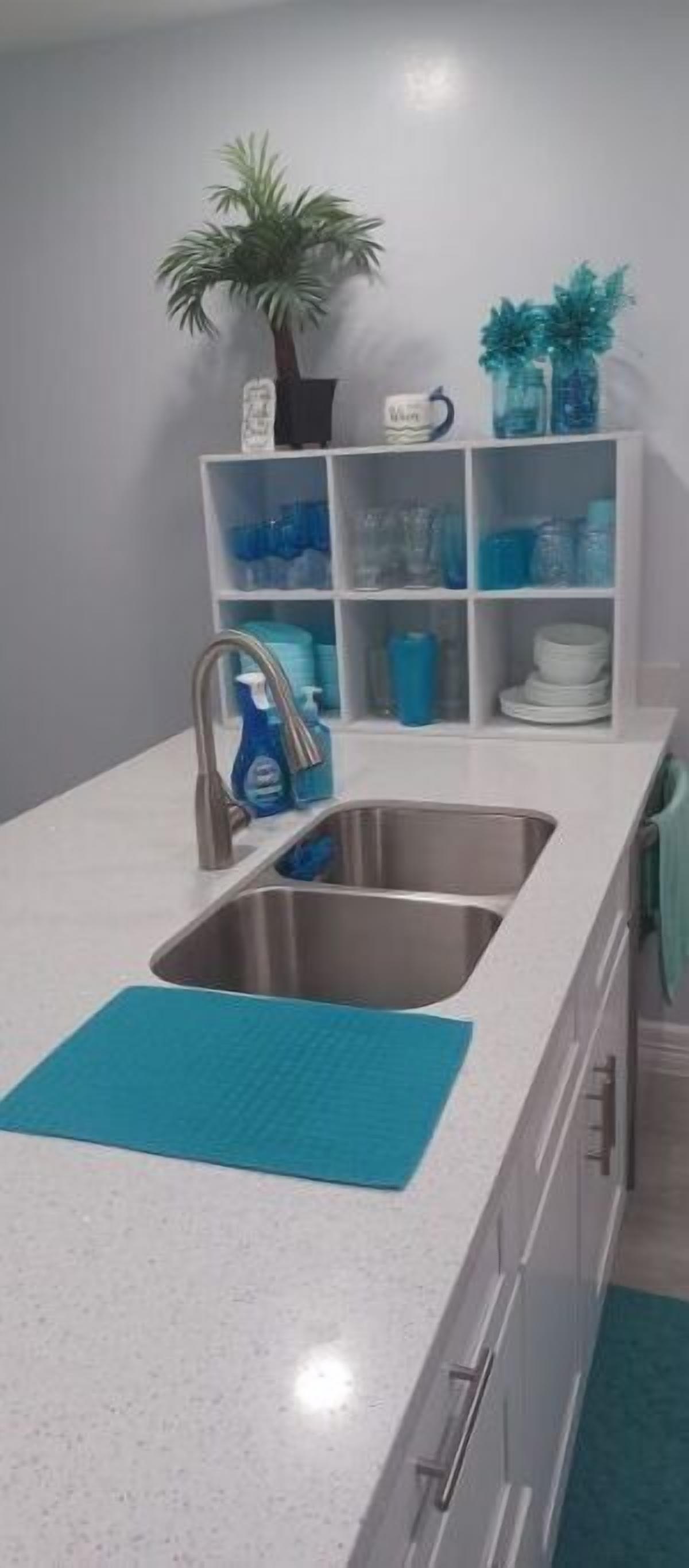A kitchen with a stainless steel sink, a blue mat, and a white countertop.