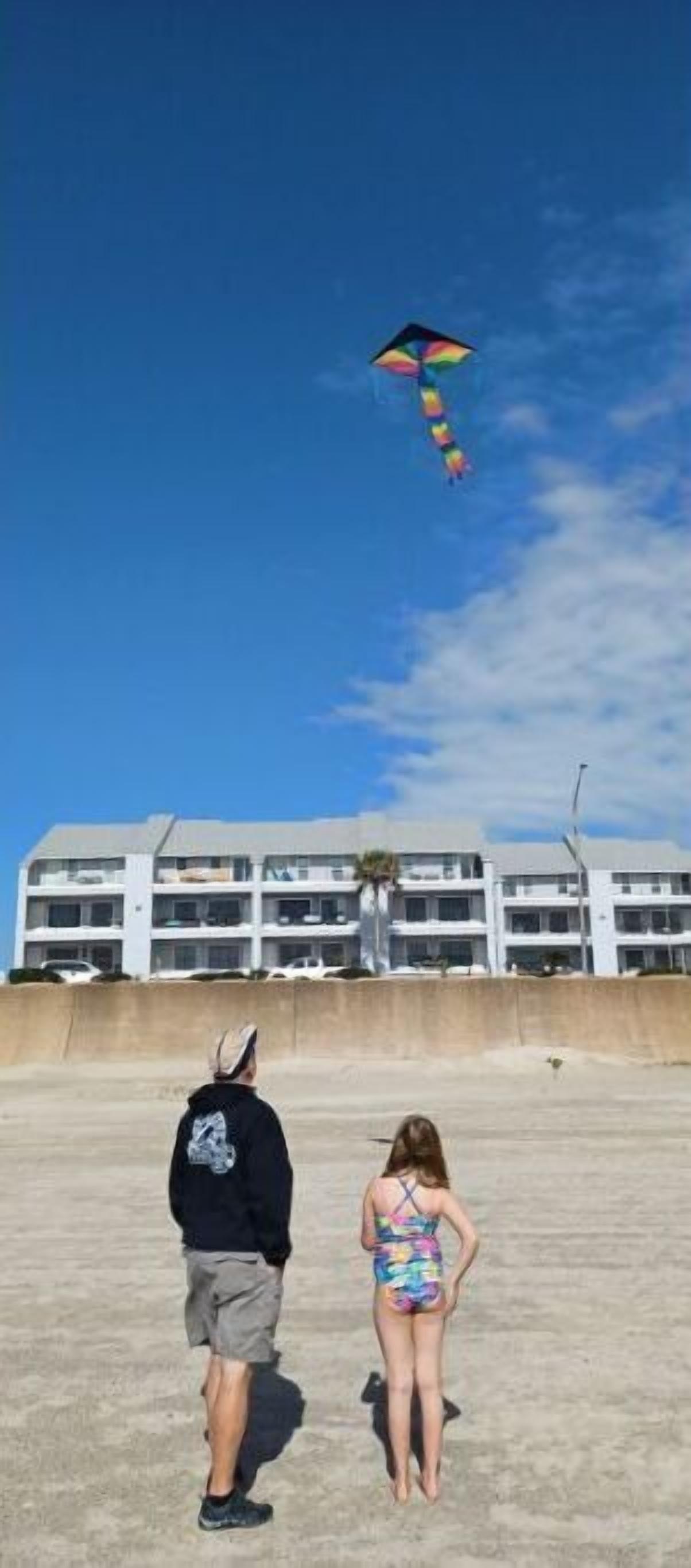 A building with multiple floors and balconies, a sandy ground, and a clear blue sky.