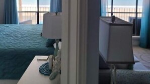 A hotel room with a bed, a desk, a lamp, and a view of the sea through large windows. - Come and Enjoy Galvestons Gem 💎  (Galveston)
