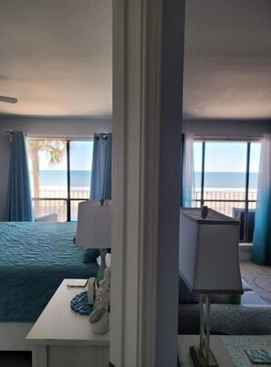 Habitación de hotel con cama, escritorio, lámpara y vista al mar a través de amplias ventanas.