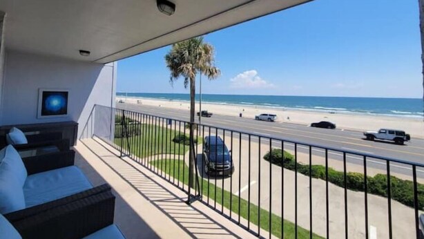 A balcony with a view of the beach and ocean, a palm tree, and a parked car. - Come and Enjoy Galvestons Gem 💎  (Galveston)