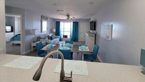 A modern living room with a sofa, a dining table with chairs, a kitchen area, and a bathroom visible through an open door. - Come and Enjoy Galvestons Gem 💎  (Galveston)
