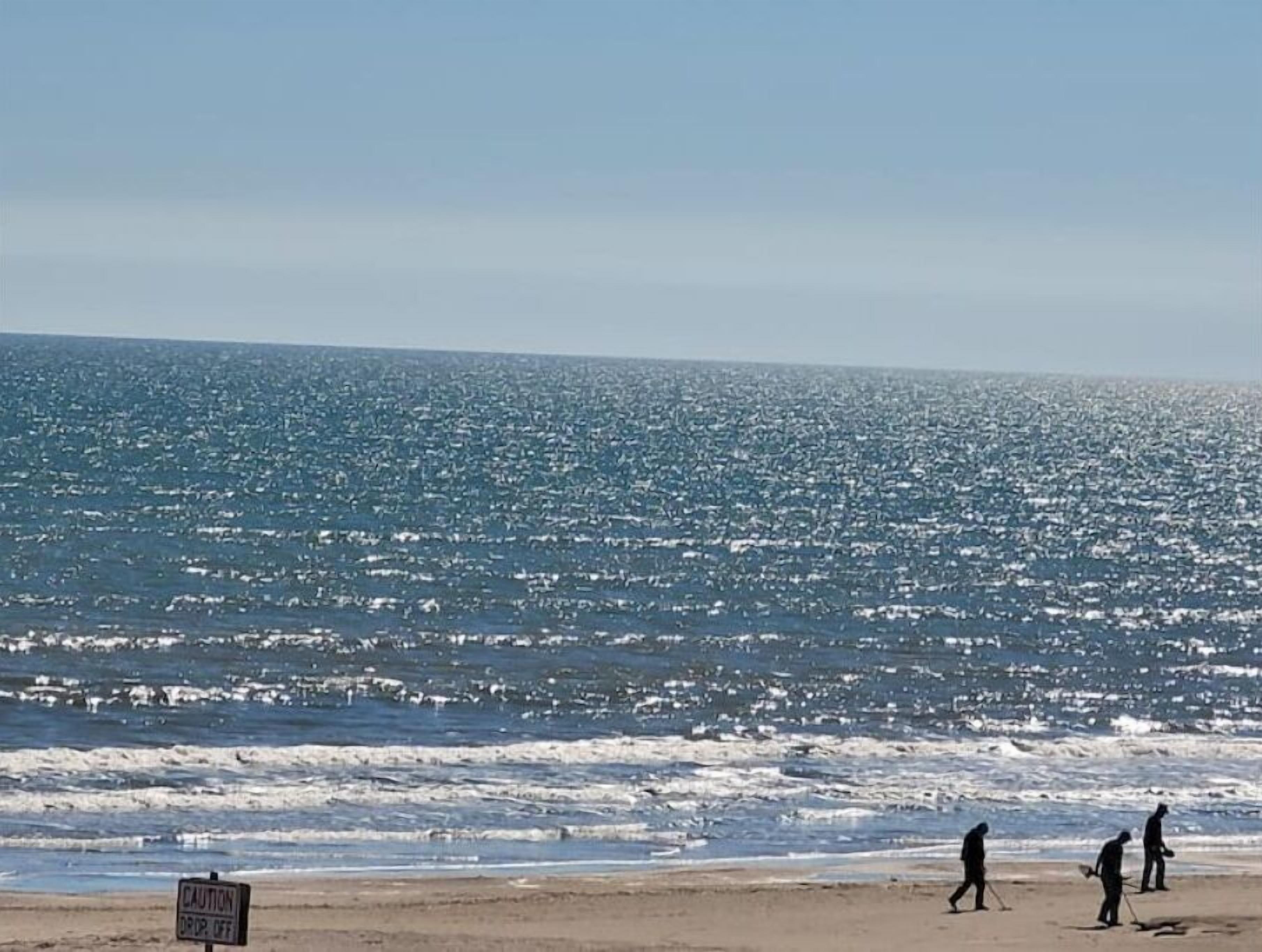 A beach with a caution sign and people walking along the shore.