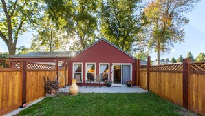 Une maison rouge avec un jardin clôturé, un grand vase et des plantes en pot.