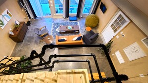 Un salon moderne avec un canapé, une table basse et des fauteuils. Un escalier avec une rampe est visible au premier plan.