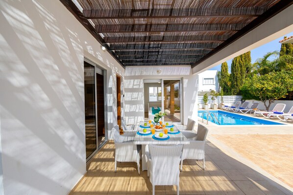 An outdoor patio with a pool, white wicker furniture, and a covered area with a patterned ceiling.
