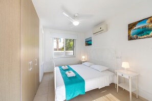 A bedroom with a bed, a window, a ceiling fan, a nightstand, and a painting on the wall.