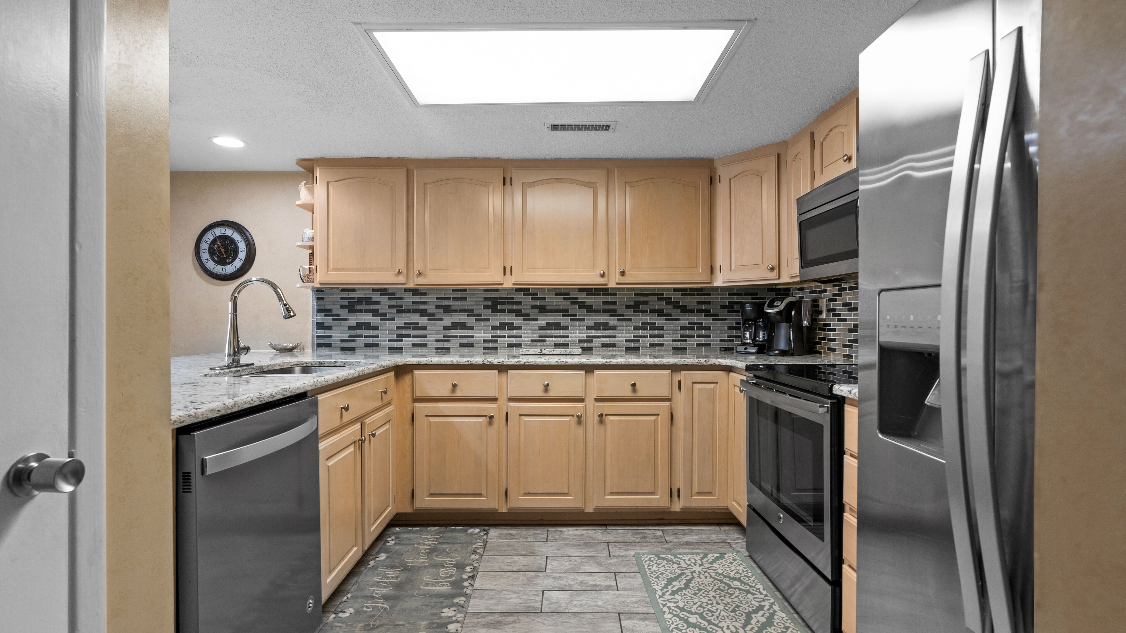 A compact kitchen with wooden cabinets, a stainless steel refrigerator, and a tiled backsplash.