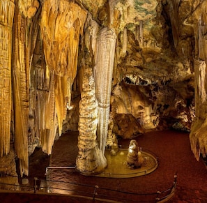 Una cueva con estalactitas y estalagmitas, una plataforma de observación circular y una pequeña estatua.