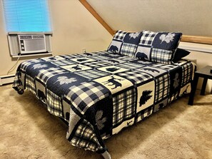 A bedroom with a checkered bedspread featuring animal prints, a bedside table, and a window with blinds. - Walk to Shenandoah River / Hiking nearby / Dog friendly (Luray)