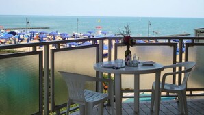Ein Balkon mit Tisch und Stühlen mit Blick auf einen Strand mit Sonnenschirmen.