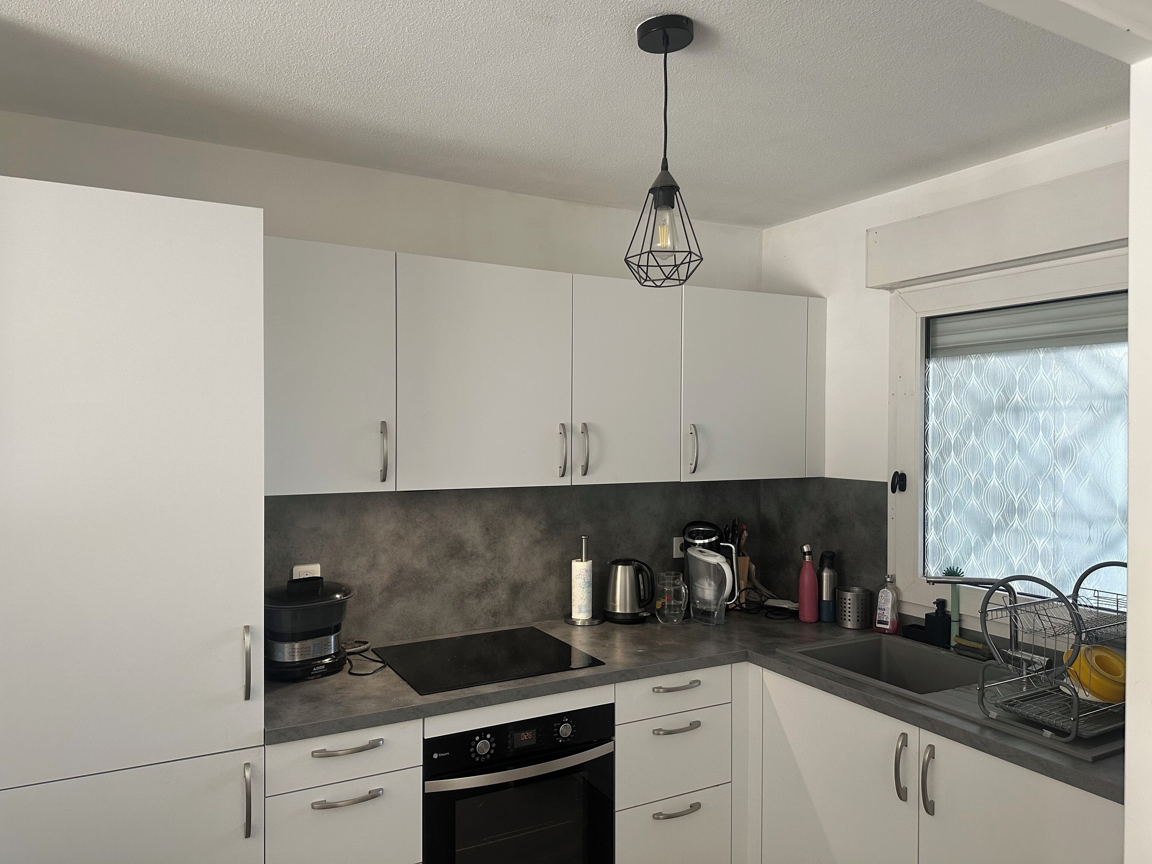 Une cuisine moderne avec des armoires blanches, un comptoir noir et un luminaire suspendu au design géométrique original.