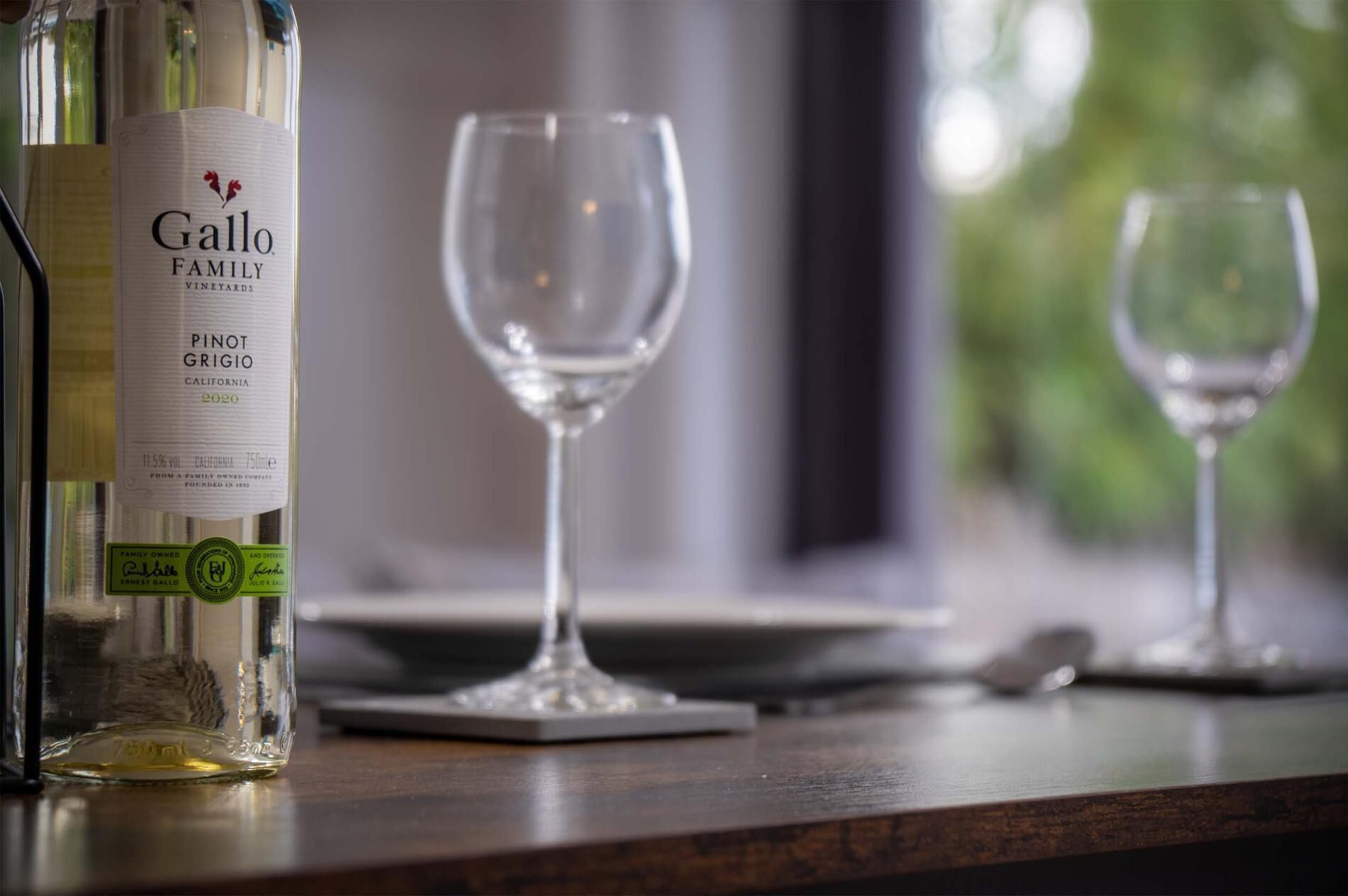 Eine Flasche Gallo Family Pinot Grigio Wein auf einem Holztisch mit zwei leeren Weingläsern.