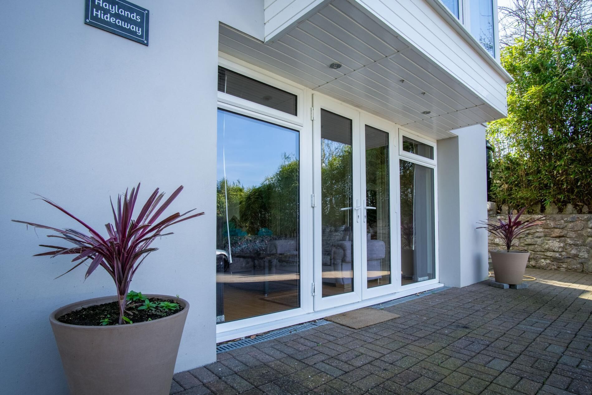 Un bâtiment moderne doté d’une grande entrée avec une porte-fenêtre coulissante, de plantes en pot et d’un mur en pierre.