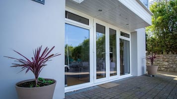 Un bâtiment moderne doté d’une grande entrée avec une porte-fenêtre coulissante, de plantes en pot et d’un mur en pierre.