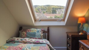 Une chambre avec un puits de lumière, un lit recouvert d’une courtepointe aux couleurs vives, une table de chevet avec une lampe et une commode.