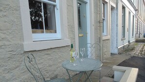 Une table en métal et deux chaises se trouvent devant un bâtiment à la façade en pierre.
