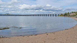 Une plage avec une longue jetée qui s’avance dans une eau calme, un ciel dégagé et des bâtiments qui se dessinent à l’horizon.