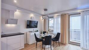 A modern kitchen with a TV, white cabinets, and a dining area with a round table and chairs. - Apartamenty Swinoujscie K Rozy Wiatrow 2 (Swinoujscie)