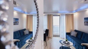 A modern living room with a blue sofa, a small round table with a plant, and a dining area with a chair and table. - Apartamenty Swinoujscie K Rozy Wiatrow 2 (Swinoujscie)