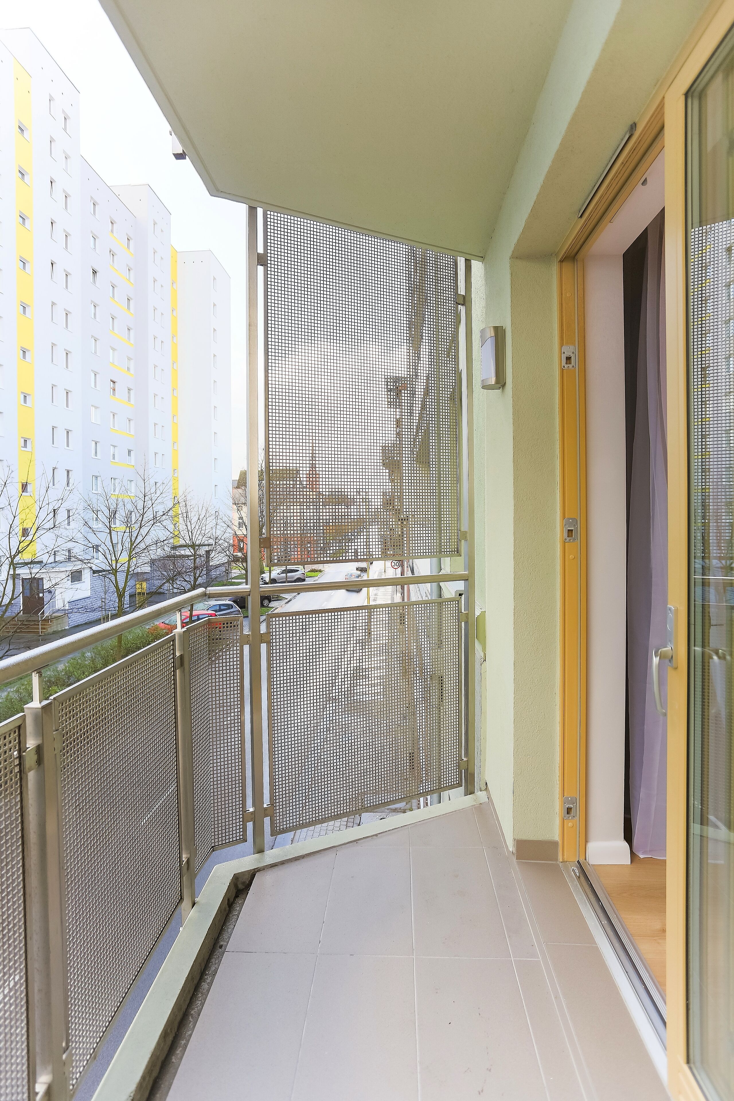 Un balcón con baranda de metal, una puerta de vidrio y vista a un edificio con varias ventanas.