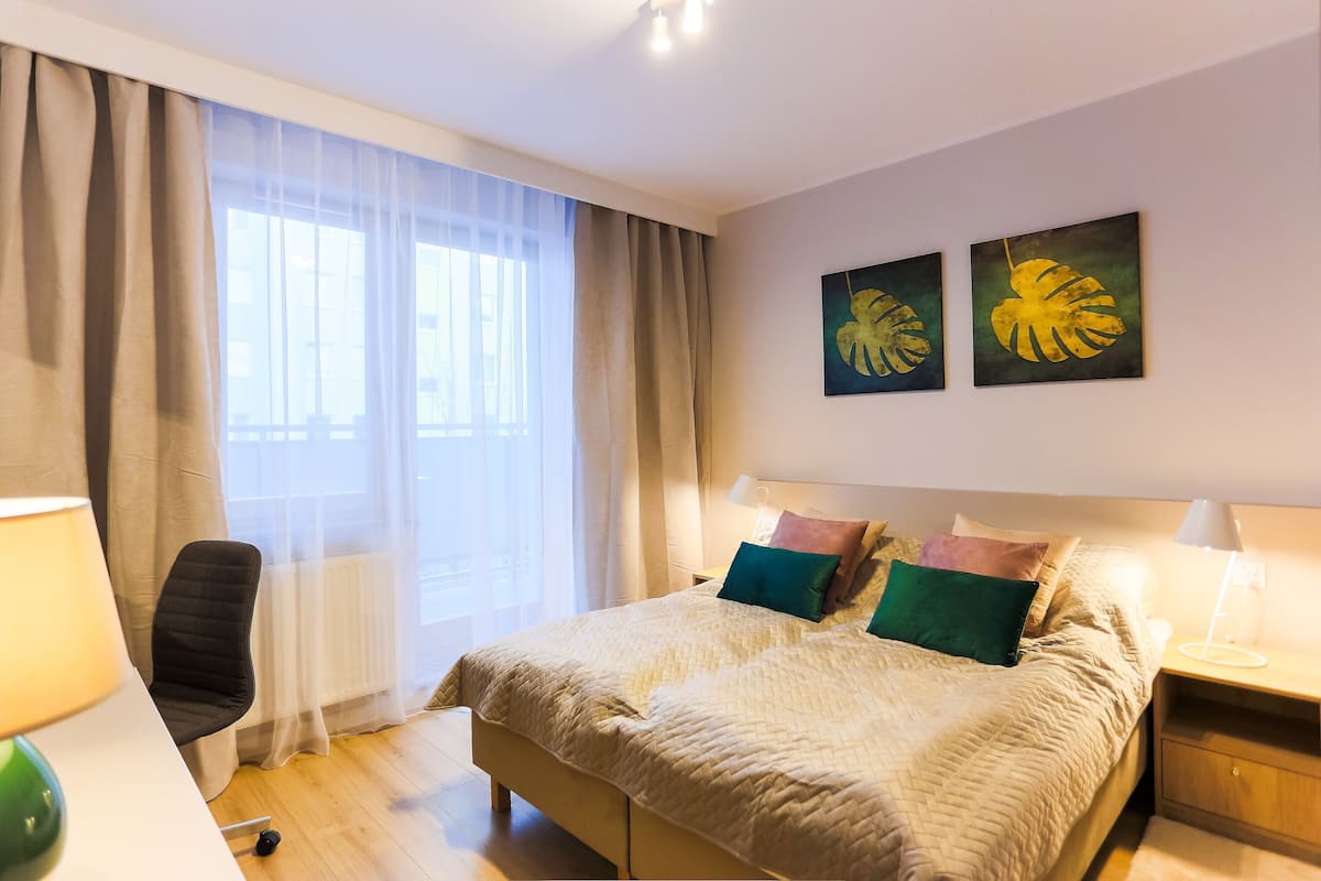 A neatly arranged bedroom with a bed, bedside lamps, a chair, and a window with curtains.
