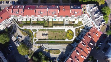 An aerial view of a residential area with red-roofed buildings, a central landscaped area, and a curved road.