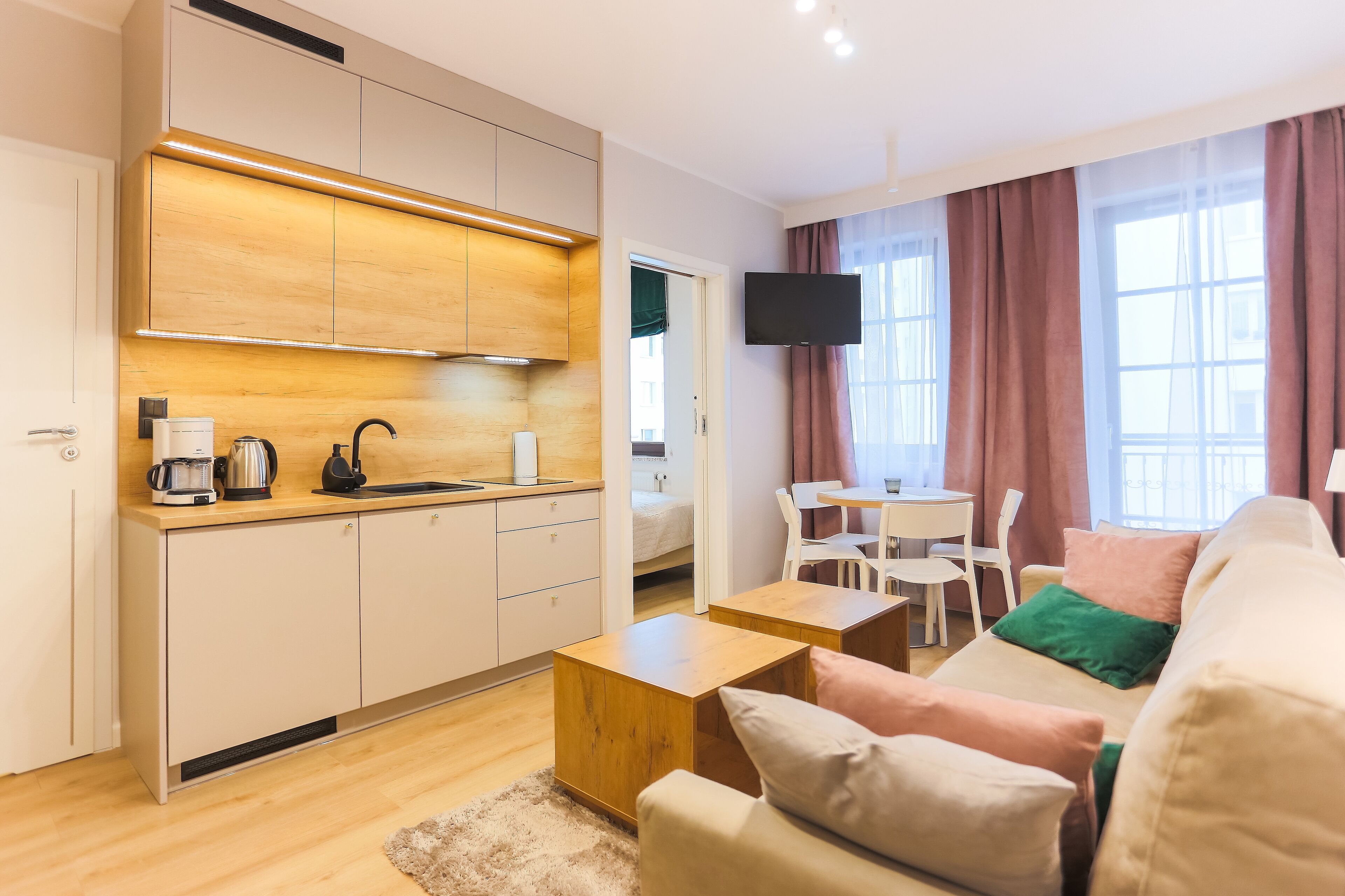 Um apartamento moderno com cozinha compacta, sala de jantar, sala de estar com sofá e televisão na parede.