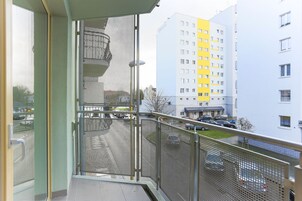 A balcony with a metal railing, a view of a parking lot, and adjacent buildings with multiple floors and balconies.