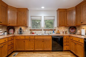 A kitchen with wooden cabinets, a dishwasher, a coffee maker, and a window with blinds. - Cozy Cottage on 140 Acres | Just 30 minutes from Tulsa (Haskell)