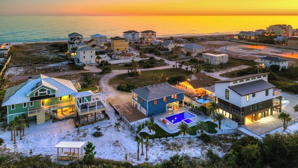Zona residencial costera con casas, una piscina y vistas al océano al atardecer.