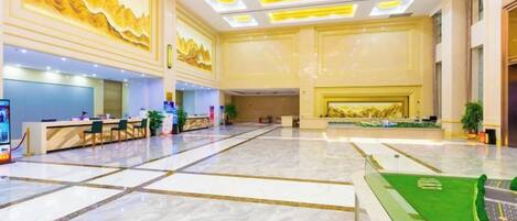 A spacious lobby with a reception desk, seating area, and a green artificial turf feature.