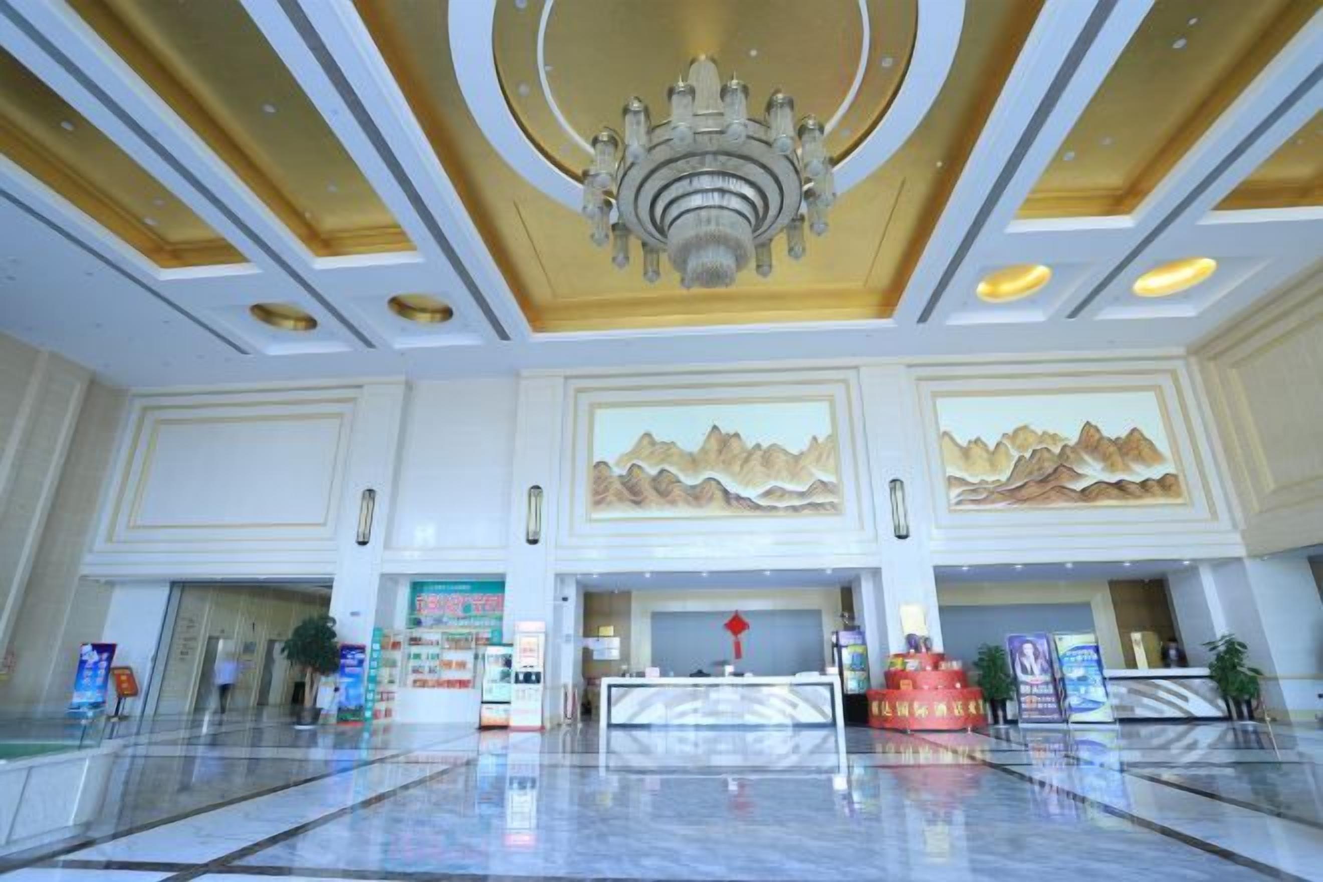 A spacious lobby with a chandelier, reception desk, and mountain artwork on the walls.