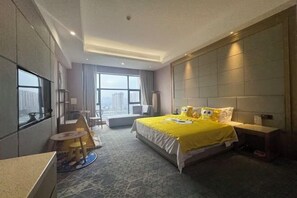 A hotel room with a large bed, a desk, a chair, and a view of the city. - Yuda International Hotel (Wuxuan)