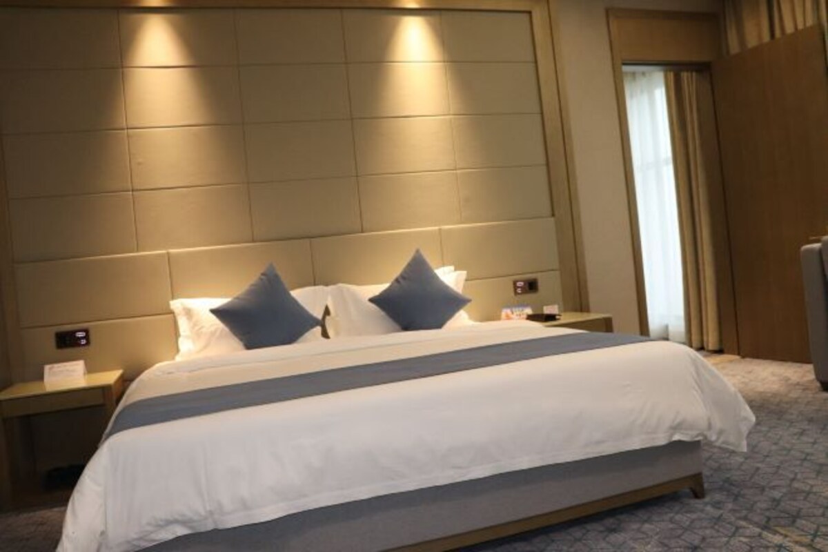 Una habitación de hotel con una cama grande, dos mesitas de noche y una ventana con cortinas.