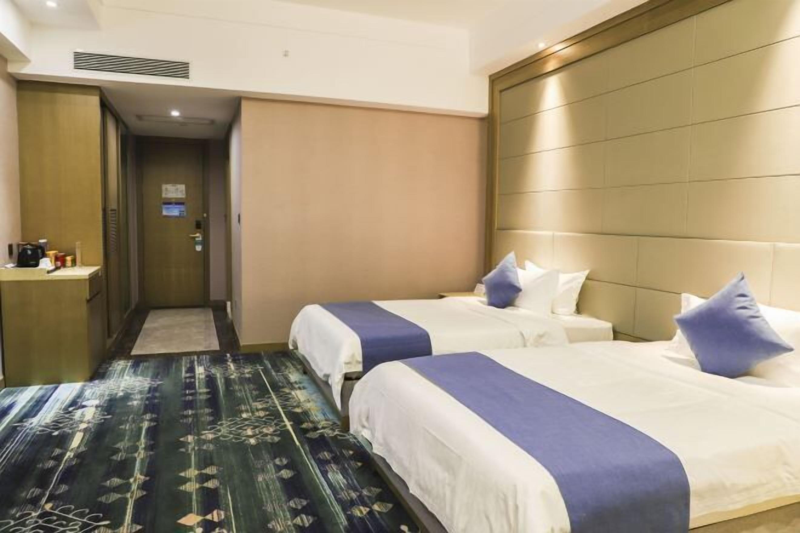 Una habitación de hotel con dos camas, una mesita de noche, un cabecero y una alfombra estampada.