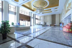Un vestíbulo amplio con piso de mármol, ventanas grandes y un candelabro central.